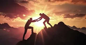 Two people helping each other climb a mountain at sunset