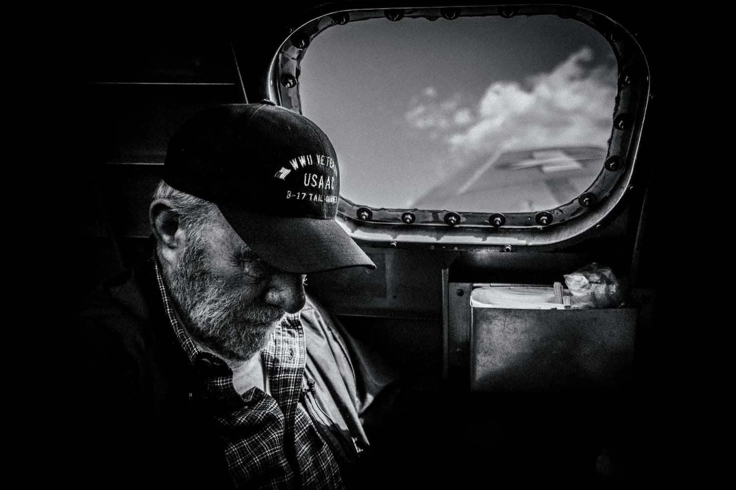 A bearded man in a military cap looking out an aircraft window